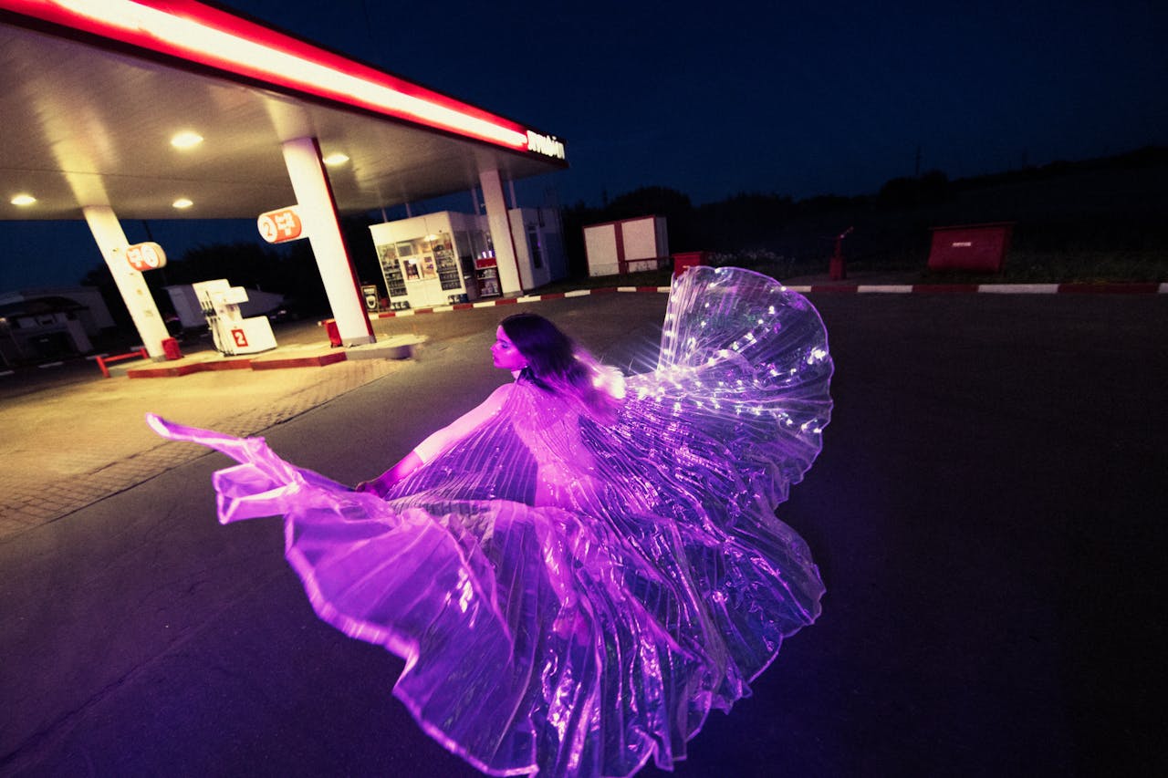 A woman dances in a glowing costume at a gas station, creating a mesmerizing night scene.