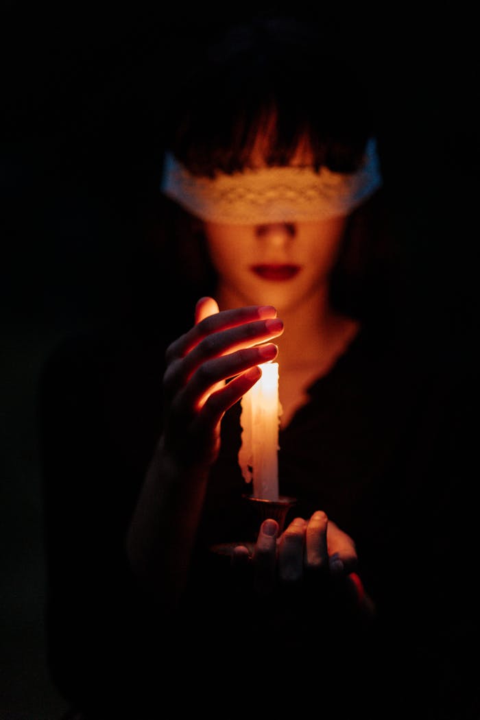 A blindfolded woman holding a lit candle in a dark setting, invoking mystery.
