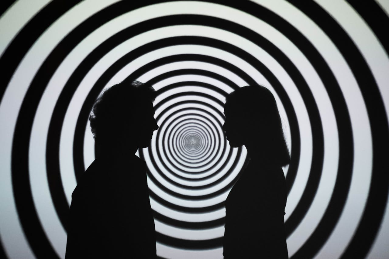 Silhouette of people facing each other with a hypnotic spiral background, creating an optical illusion.