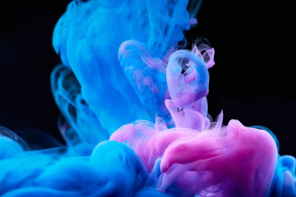 Dynamic abstract image of swirling blue and pink ink creating a colorful visual effect against a dark background.